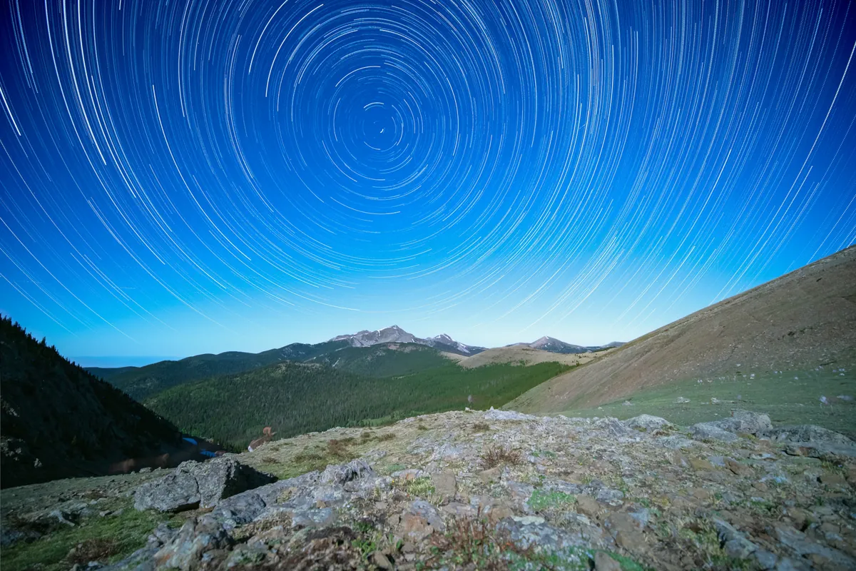 Star trails wheeling in concentric circles around the pole above a mountain ridge, under a deep blue sky.